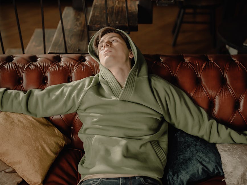 Man in a green hoodie relaxing on a leather sofa, embodying a cozy home vibe.
