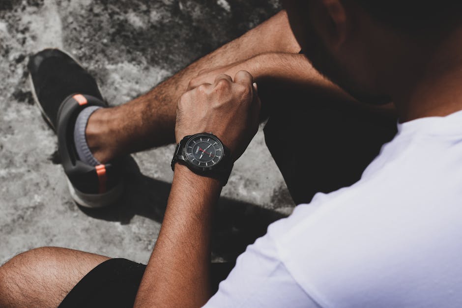 A man in casual attire checks the time on his fashionable wristwatch while sitting outdoors.