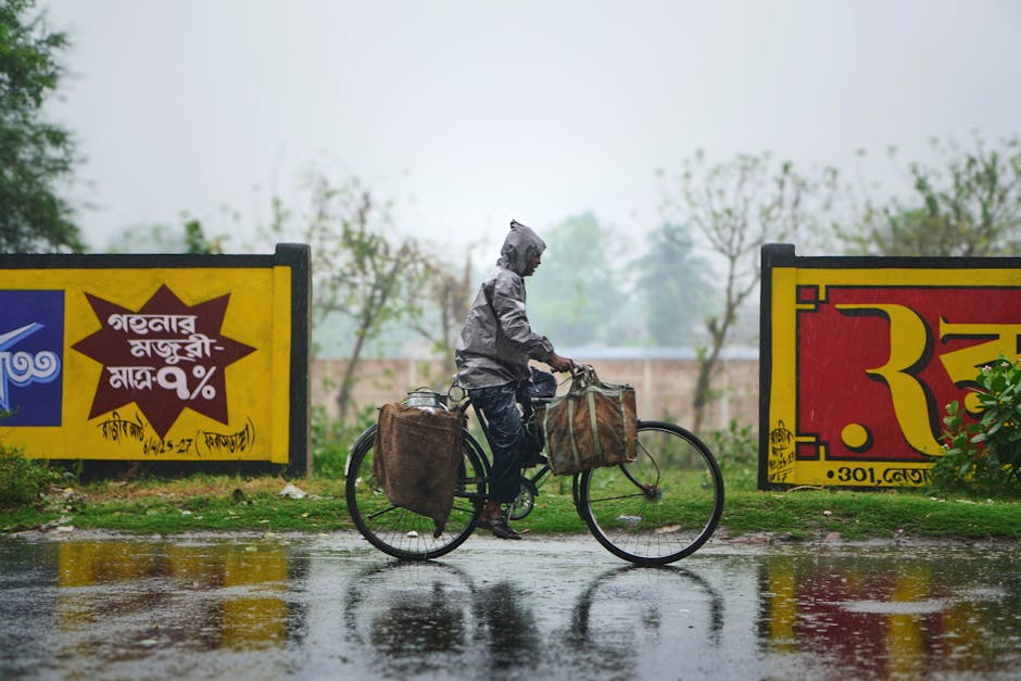A cyclist rides through the rain by vibrant advertising billboards in a city setting, creating a lively urban scene.