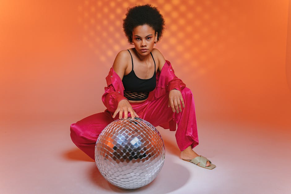 Confident woman in bright pink attire and afro hairstyle posing with a disco ball.