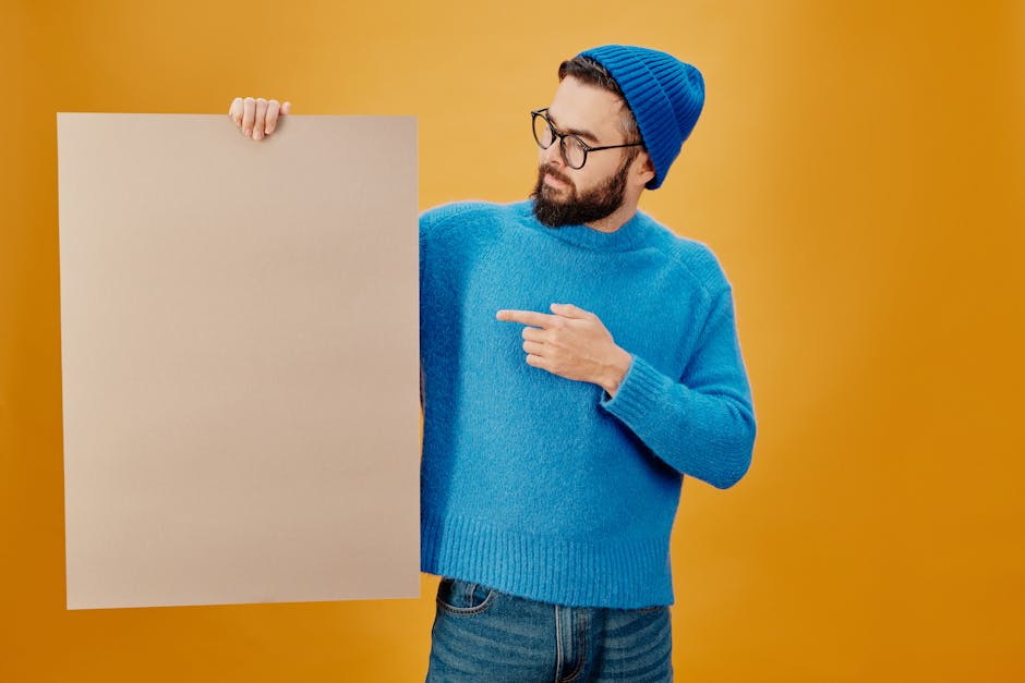 Bearded man in blue sweater and beanie holding blank paper with copy space background.